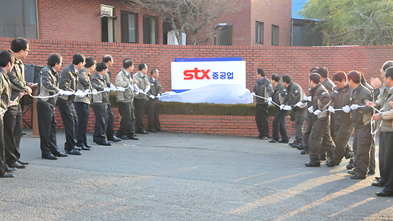 Image of STX Heavy Industries logo flanked by employees