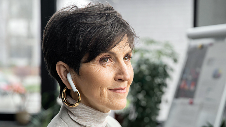 Businesswoman listening music in earbud and looking away in office