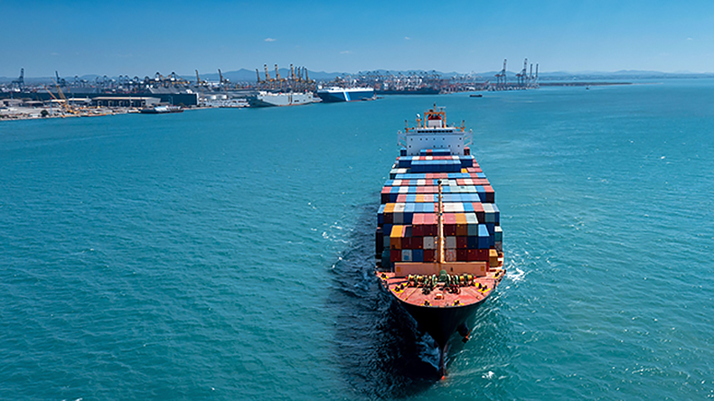 Aerial view in front of containership leaving port on a blue sea