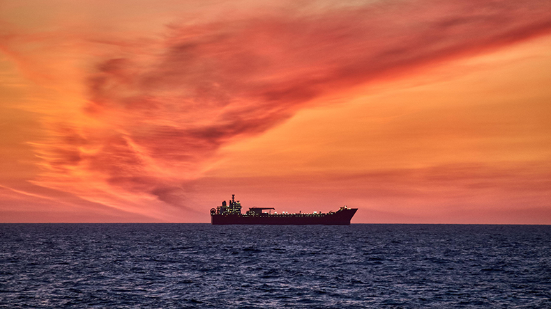 Panoramic view of colourful ocean sky, with red and orange clouds, dark sea and silhouette of a ship on the horizon