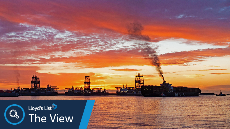Containership belches out black smoke as the sky explodes with colour as the sun rises behind drilling ships in Las Palmas port on Gran Canaria
